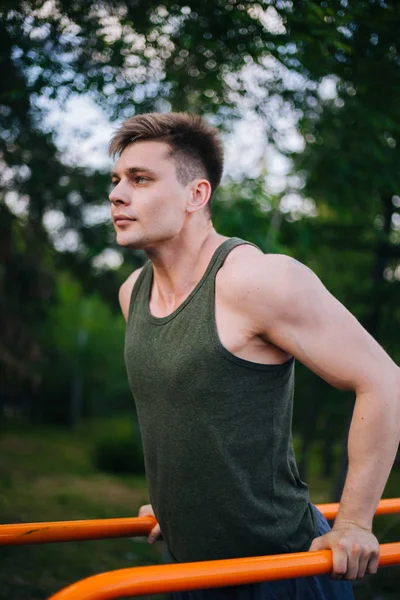 Genç yakışıklı olan bir spor yatay çubuklar üzerinde çalışmaktadır. Sağlıklı yaşam tarzı