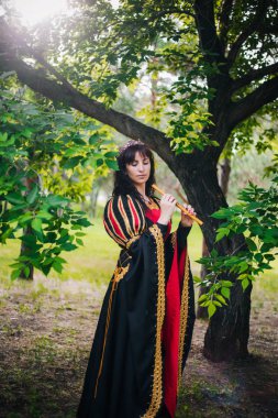 Kraliçe ile elleri bir flüt. Taç güzel kızı boru üzerinde çalış. Fantezi. Altın nakış ile Ortaçağ siyah ve kırmızı elbise.