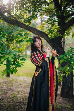 Kraliçe ile elleri bir flüt. Taç güzel kızı boru üzerinde çalış. Fantezi. Altın nakış ile Ortaçağ siyah ve kırmızı elbise.