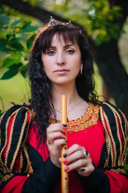 Kraliçe ile elleri bir flüt. Taç güzel kızı boru üzerinde çalış. Fantezi. Altın nakış ile Ortaçağ siyah ve kırmızı elbise.