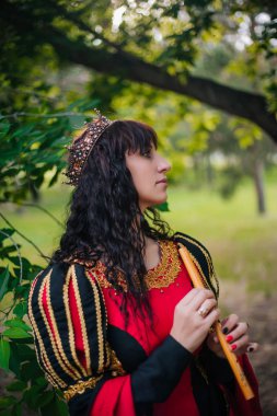 Kraliçe ile elleri bir flüt. Taç güzel kızı boru üzerinde çalış. Fantezi. Altın nakış ile Ortaçağ siyah ve kırmızı elbise.