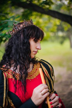 Kraliçe ile elleri bir flüt. Taç güzel kızı boru üzerinde çalış. Fantezi. Altın nakış ile Ortaçağ siyah ve kırmızı elbise.