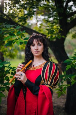 Kraliçe ile elleri bir flüt. Taç güzel kızı boru üzerinde çalış. Fantezi. Altın nakış ile Ortaçağ siyah ve kırmızı elbise.