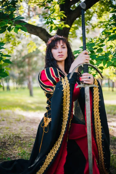 彼女は両手で剣を持つ女王 王冠の美しい少女 ファンタジー ゴールドの刺繍と中世の黒と赤のドレス — ストック写真