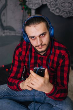 Noel şöminesinin arkasında oturan adam akıllı telefonundan müzik dinliyor.