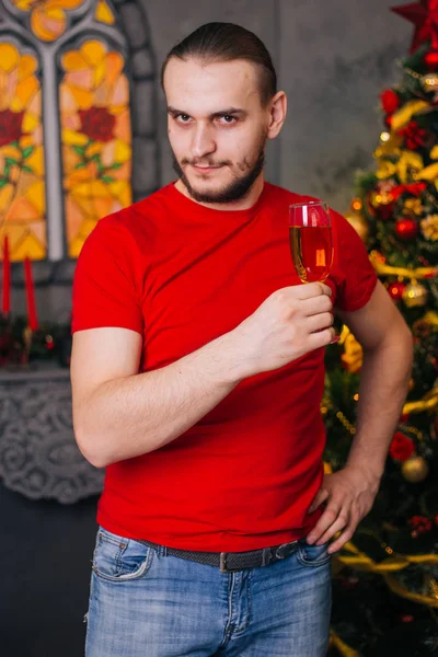 赤いTシャツを着た髭を生やした男が 贈り物を手にし シャンパンを飲みながら お祭り気分 新年の準備 クリスマスインテリア — ストック写真