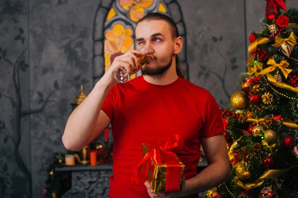 一个留着胡子 穿着红色T恤 手里拿着礼物和香槟的男人 喜庆的心情 迎接新的一年 圣诞内部 — 图库照片