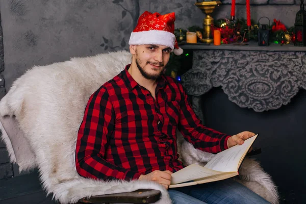 Guy Red Hat Santa Claus Sits Chair Fireplace Man Holds — Stock Photo, Image