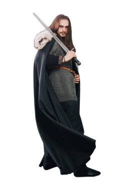 A knight in chain mail and with a fur collar in a black cloak on a white background in full growth. Viking man with long hair and a beard in armor holds a sword.