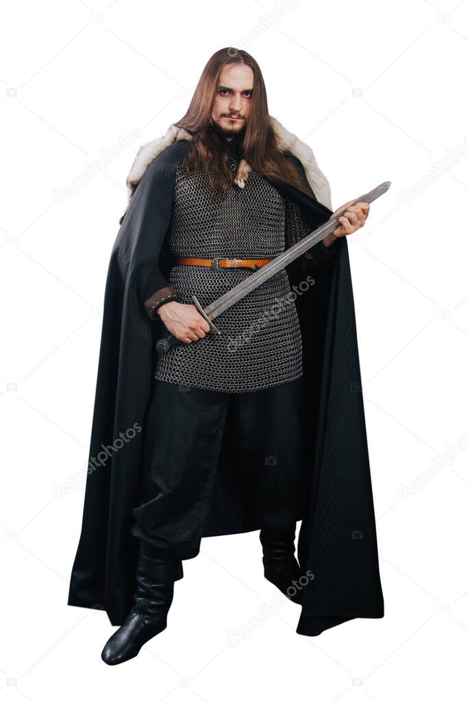 A knight in chain mail and with a fur collar in a black cloak on a white background in full growth. Viking man with long hair and a beard in armor holds a sword.