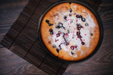 Berry pie sprinkled with icing sugar and pink sweet hearts.