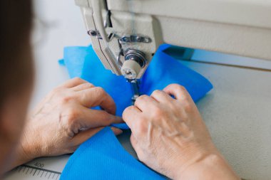 Stepwise stitching of blue fabric medical masks on a sewing machine. A close up of an industrial sewing machine makes a seam.