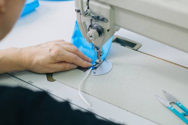 Stepwise stitching of blue fabric medical masks on a sewing machine. A close up of an industrial sewing machine makes a seam.
