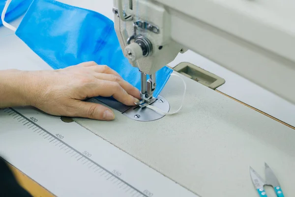 Stepwise stitching of blue fabric medical masks on a sewing machine. A close up of an industrial sewing machine makes a seam.