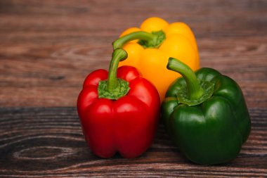 Sweet pepper multicolored on a dark wooden background. Red, yellow and green peppers are on the table.