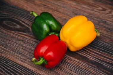 Sweet pepper multicolored on a dark wooden background. Red, yellow and green peppers are on the table.