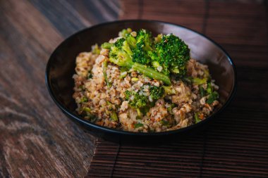 Ready buckwheat in a dark cup with vegetables. Broccoli and young beans in buckwheat.
