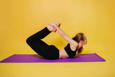Athletic, beautiful young girl practicing yoga, makes the pose of dhanurasana.