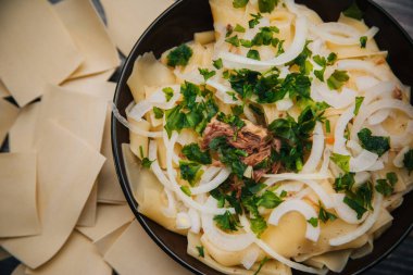 Beshbarmak in a dark plate, on a light wooden table. Dish of pastry with meat.