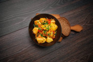 Stewed potatoes with cabbage in a dark plate on a brown wooden table.