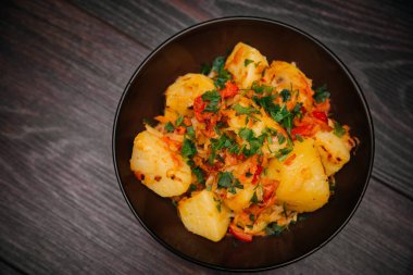 Stewed potatoes with cabbage in a dark plate on a brown wooden table.