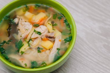 Green plate with noodle soup. With poultry meat on a light wooden table. Dietary Chicken Soup.