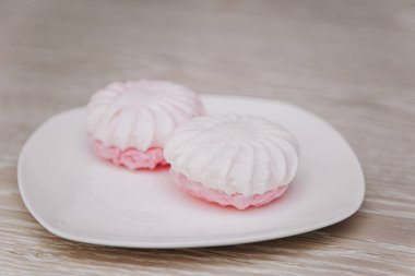 White plate with pink marshmallows on a light table.