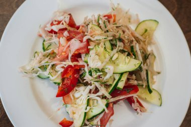 Beyaz tabakta vejetaryen lahana, salatalık ve domates salatası. Çanak koyu ahşap bir arka planda duruyor. Sağlıklı beslenme.