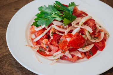 Domatesli ve soğanlı vejetaryen salatası ve beyaz tabakta otlar. Çanak koyu ahşap bir arka planda duruyor. Sağlıklı beslenme.