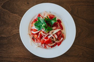 Domatesli ve soğanlı vejetaryen salatası ve beyaz tabakta otlar. Çanak koyu ahşap bir arka planda duruyor. Sağlıklı beslenme.