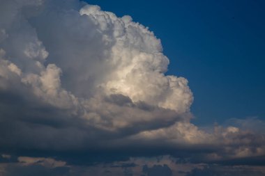 A majestic cumulus cloud dominates a clear blue sky, with dark storm clouds gathering beneath it, creating a visually stunning contrast.