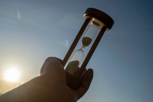 Old hourglass in a man\'s hand on a background of the sky at sunset