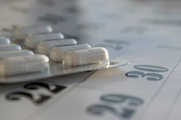 Conceptual photo with pills. White pills on a calendar background.