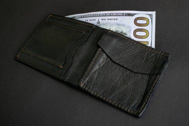 Yüz dolarlık banknotu olan siyah deri bir cüzdan. Siyah bir arka planda izole siyah cüzdan ve yakın plan para.