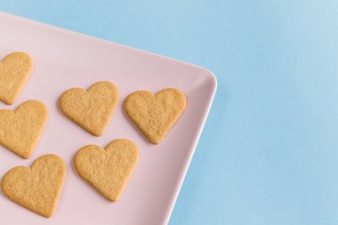Pembe tepside kalp şeklinde kurabiyeler ve açık mavi arka plan. Boşluğu kopyala.