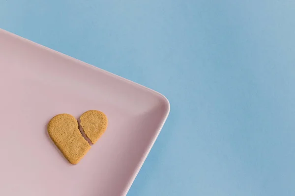 Broken heart. Heart shaped cookie isolated on a pink tray. Light blue background. Copy space