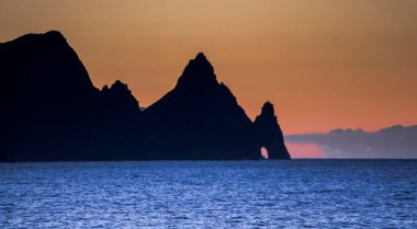 Madeira adasında gün batımı. Sahildeki kayalar, siluetler, turuncu gökyüzü ve yoğun mavi su.