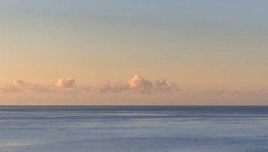 Gün batımında sakin bir deniz ve ufukta küçük bulutlar.