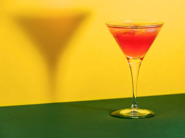緑と黄色の背景にその影を形作るガラスの中の赤いカクテル — ストック写真