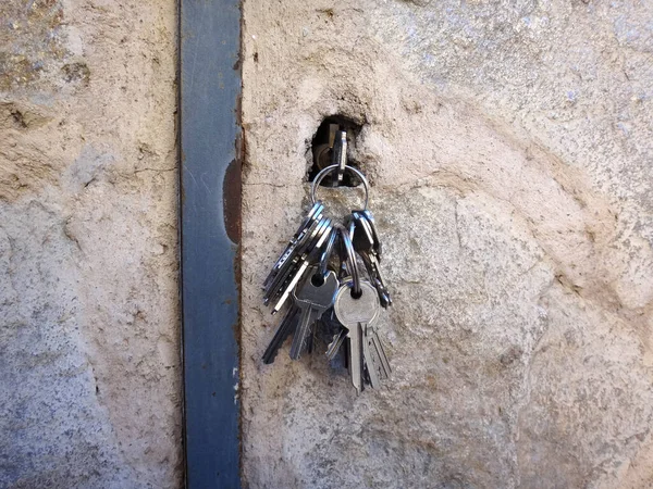 成捆的许多钥匙被插入门的钥匙孔 具有石质质感 有通往街道的办公空间 — 图库照片
