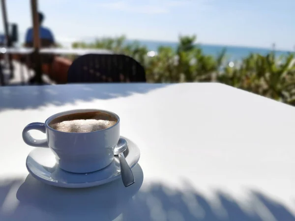 A cup of coffee against the backdrop of the sea and a coastal cafe. Spanish summer on the Mediterranean