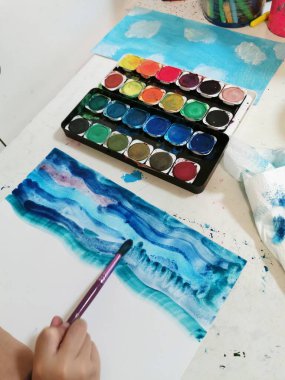 Suluboya palet ve çocuğun eli beyaz kağıda boyamak için fırça tutuyor. Denizi plastikten uzak tutmak, gezegeni güvende tutmak. çocuk eğitimi