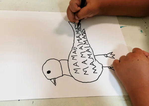 child\'s hand drawing a bird and writing to mom mama