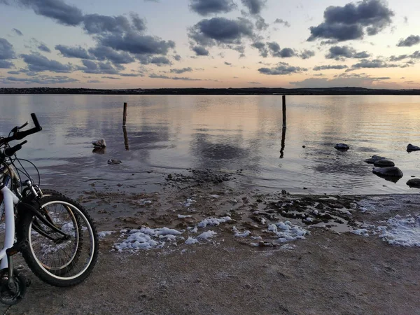 Sunset on a salt lake with a reflection of clouds on the surface and foam on the shore of the lake. Two front wheels of the bike in the foreground
