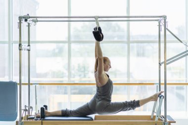Genç kadın pilates yatağında geriniyor..