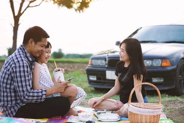 Happy asian family on picnic outdoors with car