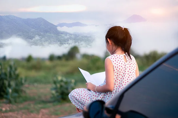 小さな子供の女の子座っているとリラックス車の中で本を読んで緑の自然背景 — ストック写真