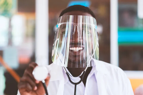 African doctor wear face shield and holding stethoscope with kind and smiling