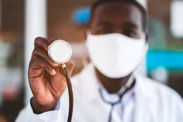 Afrikalı doktor yüz maskesi takıyor ve elinde steteskopla gülümsüyor.