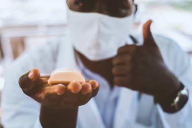 Afrikalı doktor bir sabun parçası tutuyor ve maske takıyor.